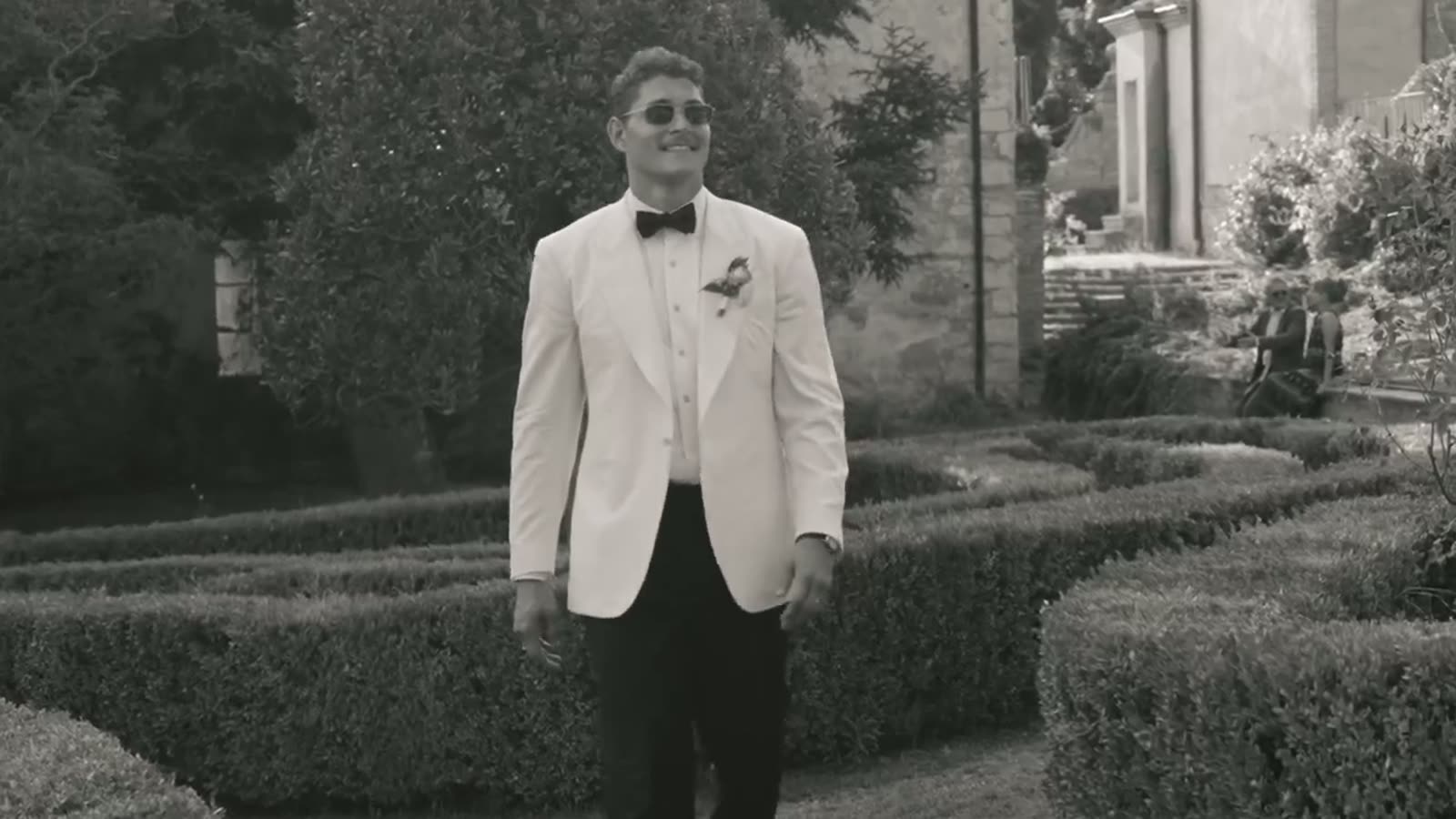 The groom in a white dinner jacket standing among the clipped hedges of the Tuscan villa garden